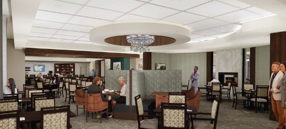 Spacious senior living dining room with booths, fireplace, modern chandeliers, and residents enjoying conversation.