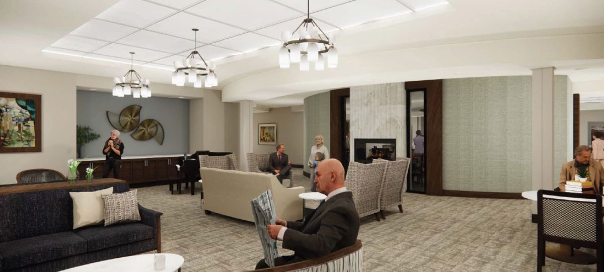 Comfortable community living room with fireplace, lounge seating, artwork, and residents relaxing and reading.