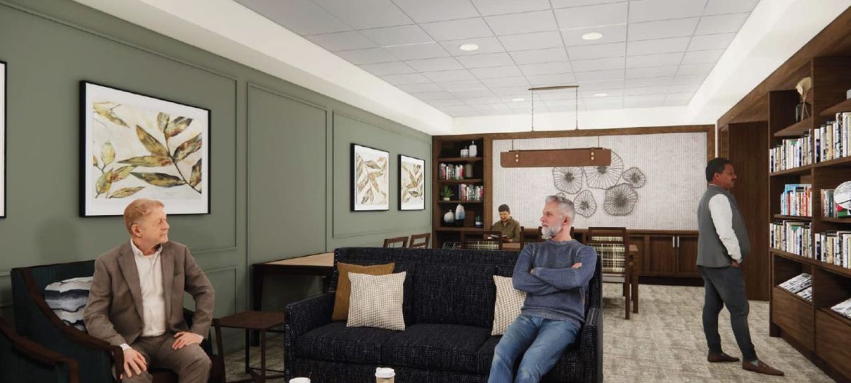 Cozy media lounge with built-in bookshelves, framed artwork, upholstered seating, and residents reading and chatting.