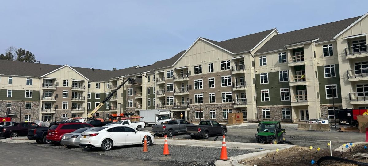 Wide view of finished apartment complex with parked vehicles, construction equipment, and workers on site
