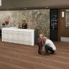 Modern lobby reception desk with staff member assisting, a child with an adult nearby, and a waiting area in the background.