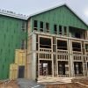 Close-up of apartment building under construction showing wooden framing, concrete base, and green exterior sheathing