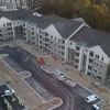 Aerial view of newly built apartment complex with parking lot, construction crew, and landscaped surroundings.